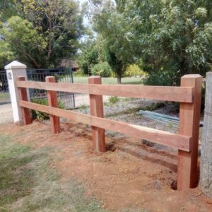 a photo of a two rail face-fixed post and rail fence, unfinished timber.